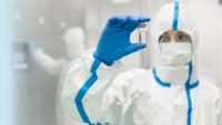 Lab tech with full-body suit while handling a clear chemical